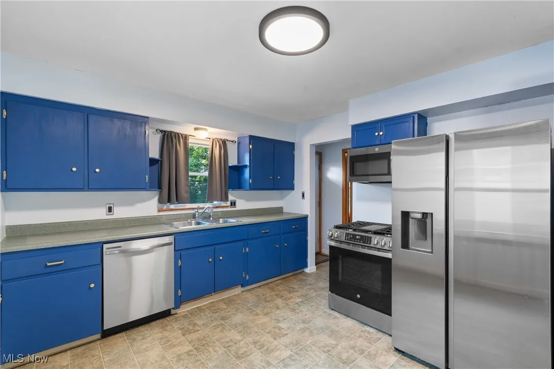 Kitchen with appliances with stainless steel finishes, blue cabinetry, and light countertops
