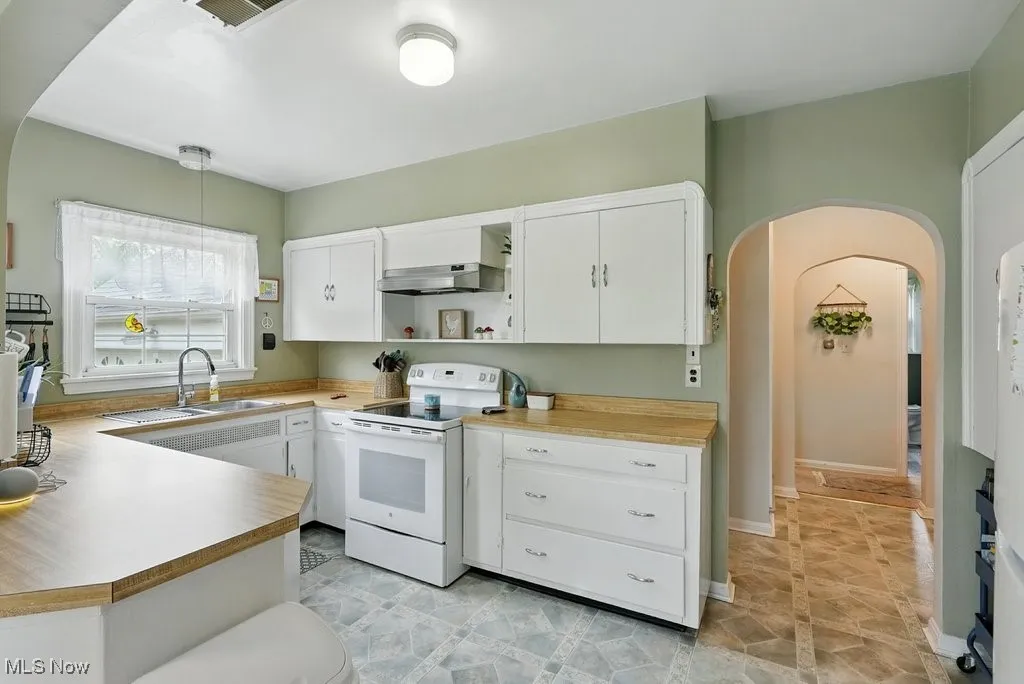 Kitchen with white range with electric cooktop, range hood, open shelves, arched walkways, and white cabinets