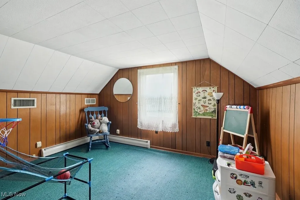 Unfurnished room featuring carpet flooring, vaulted ceiling, wood walls, and a baseboard radiator