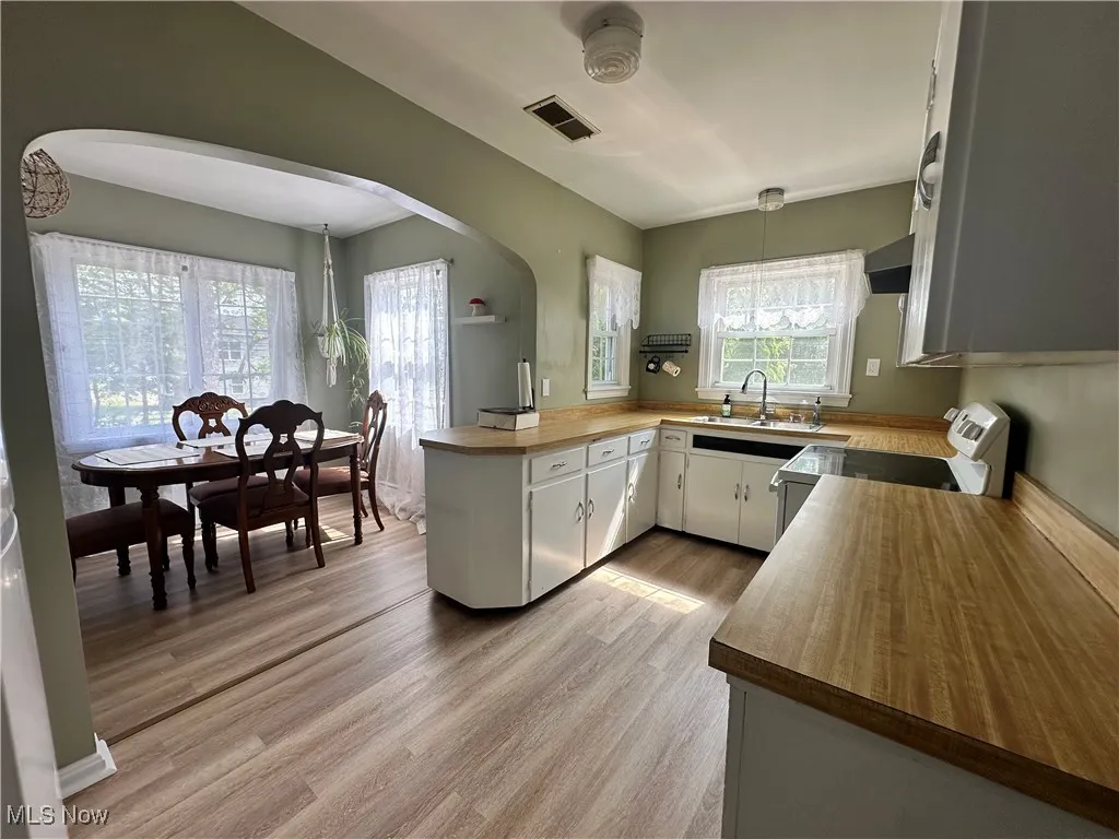 Kitchen featuring white electric range oven, arched walkways, wooden counters, light wood-style floors, and a peninsula