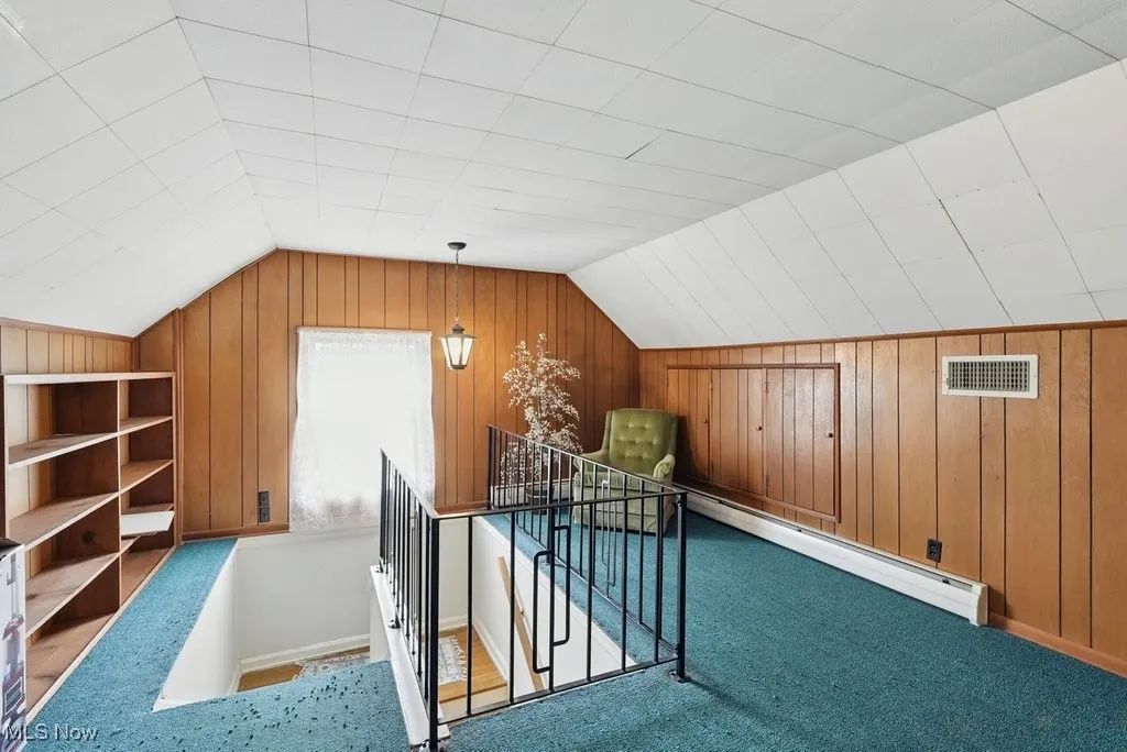 Additional living space featuring lofted ceiling, a baseboard radiator, wooden walls, and carpet flooring