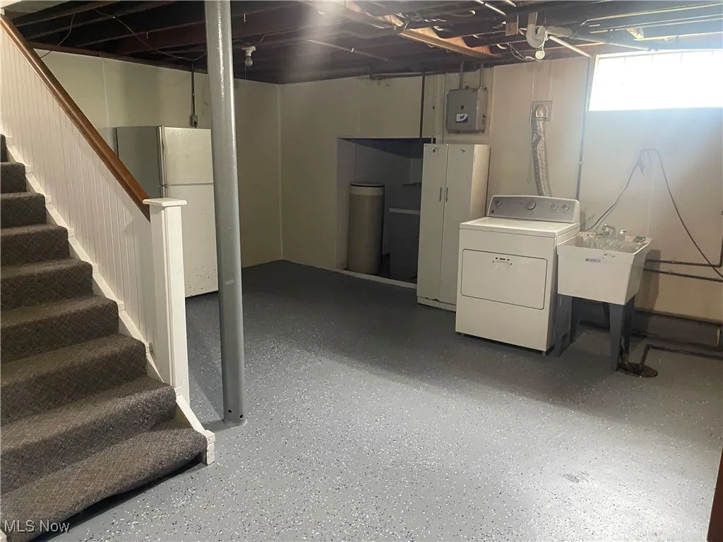 Below grade area featuring dryer, stairway, electric panel, and freestanding refrigerator