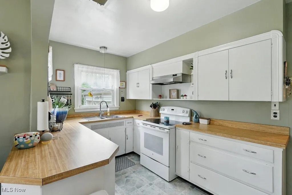 Kitchen with electric stove, open shelves, white cabinetry, ventilation hood, and light countertops