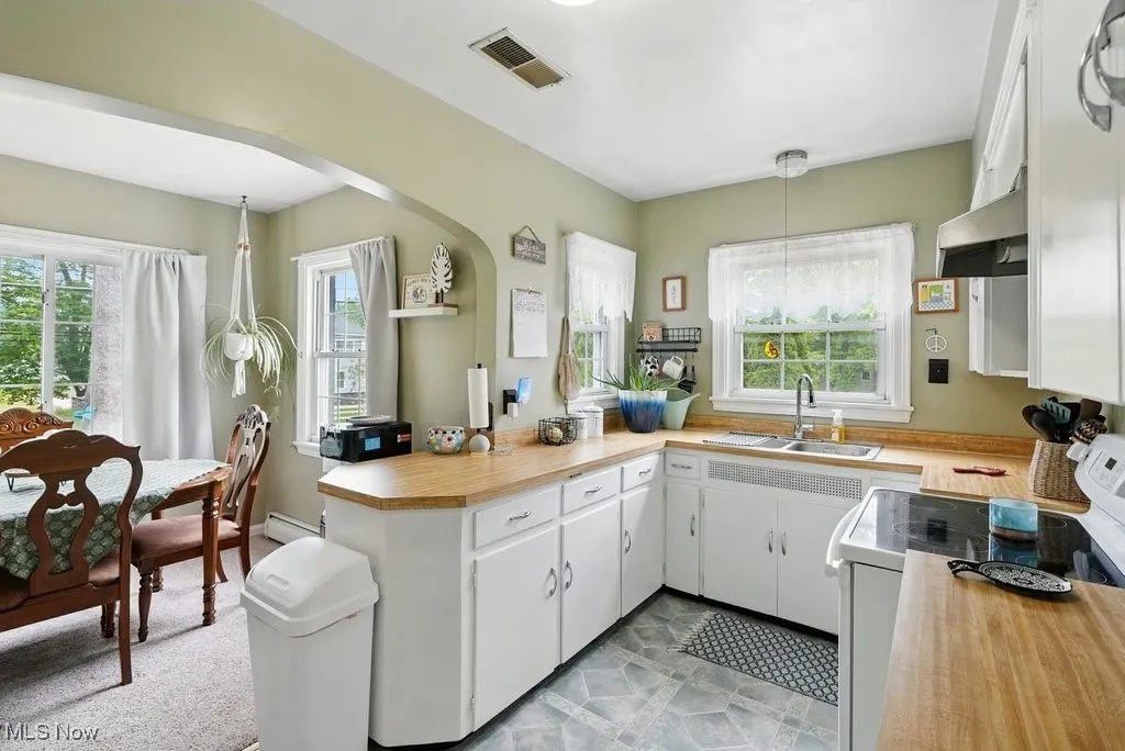 Kitchen featuring white electric stove, under cabinet range hood, a peninsula, and butcher block counters