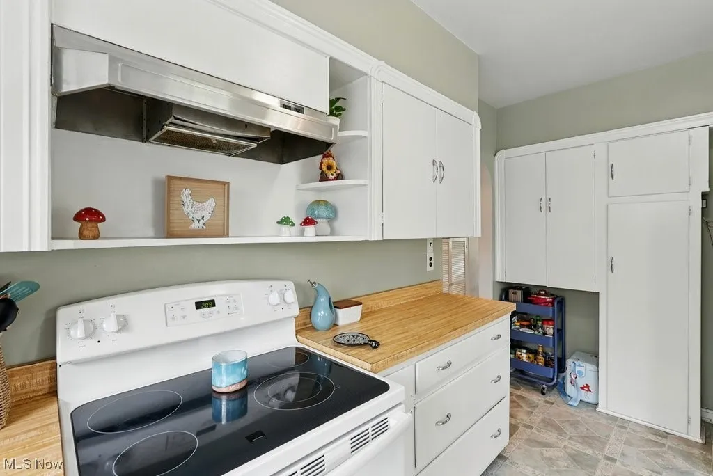 Kitchen with white electric stove, open shelves, extractor fan, light countertops, and white cabinets