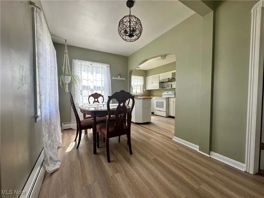 Dining area featuring arched walkways, light wood-type flooring, and a baseboard radiator