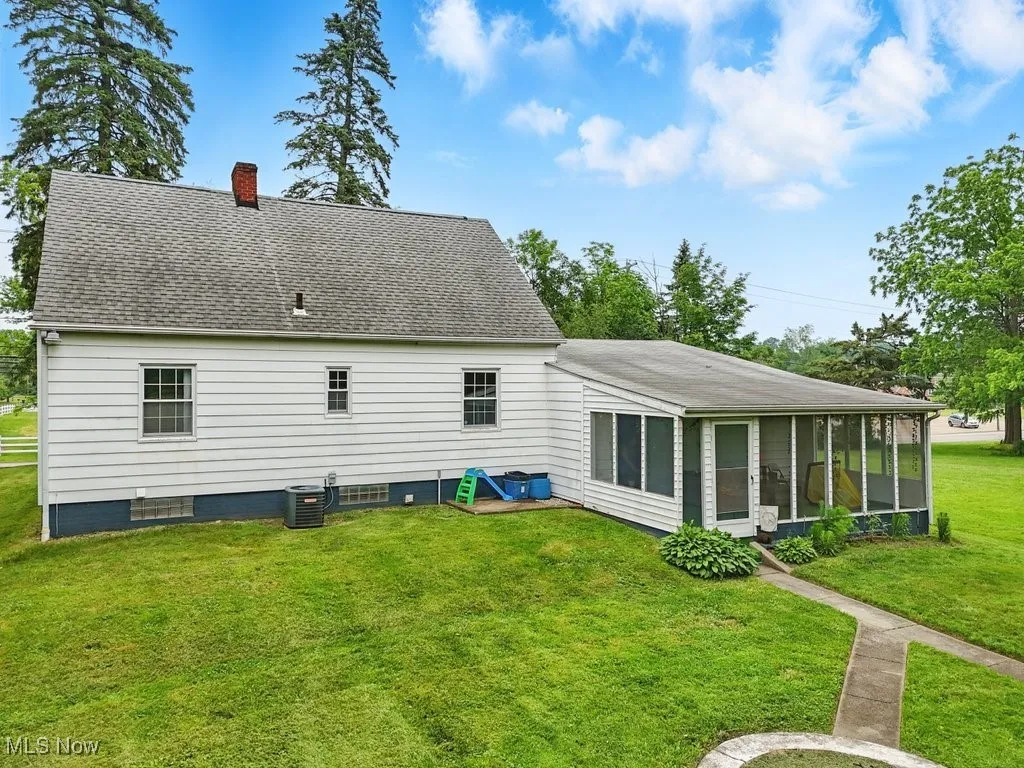 Rear view of house featuring a sunroom, a chimney, a yard, and roof with shingles