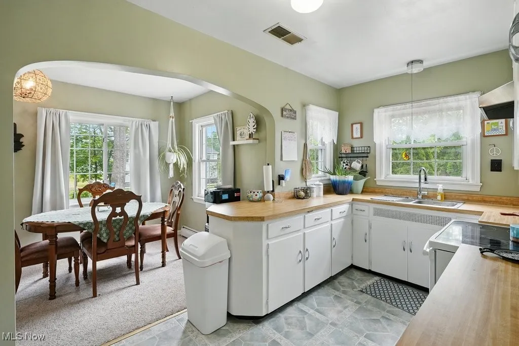 Kitchen featuring arched walkways, light countertops, white cabinets, a peninsula, and hanging light fixtures