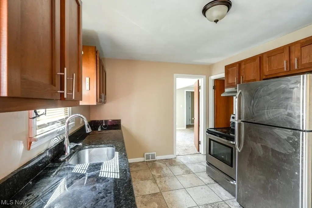 Kitchen with stainless steel appliances, under cabinet range hood, brown cabinets, and dark stone counters