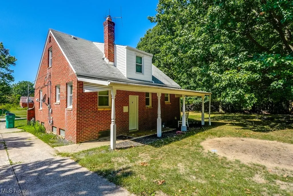 View of front facade featuring brick siding, a front lawn, a chimney, and a shingled roof
