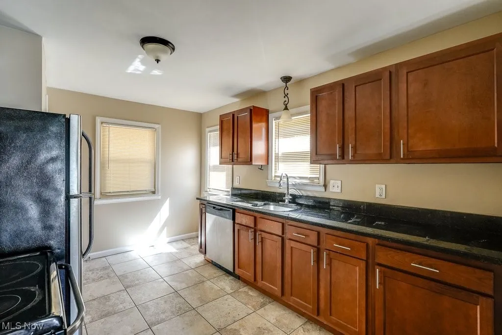 Kitchen featuring appliances with stainless steel finishes, dark stone countertops, brown cabinetry, and pendant lighting