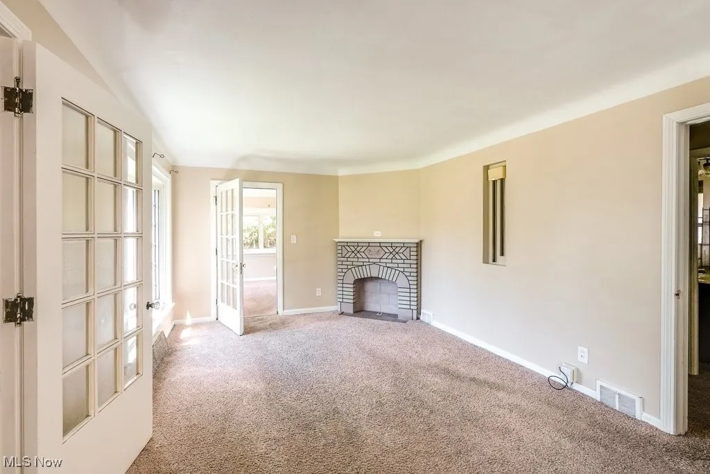 Unfurnished living room with carpet floors, a fireplace, and french doors