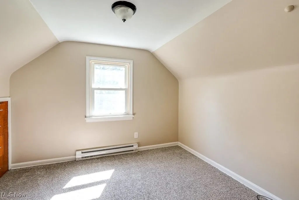 Additional living space with baseboard heating, vaulted ceiling, and carpet