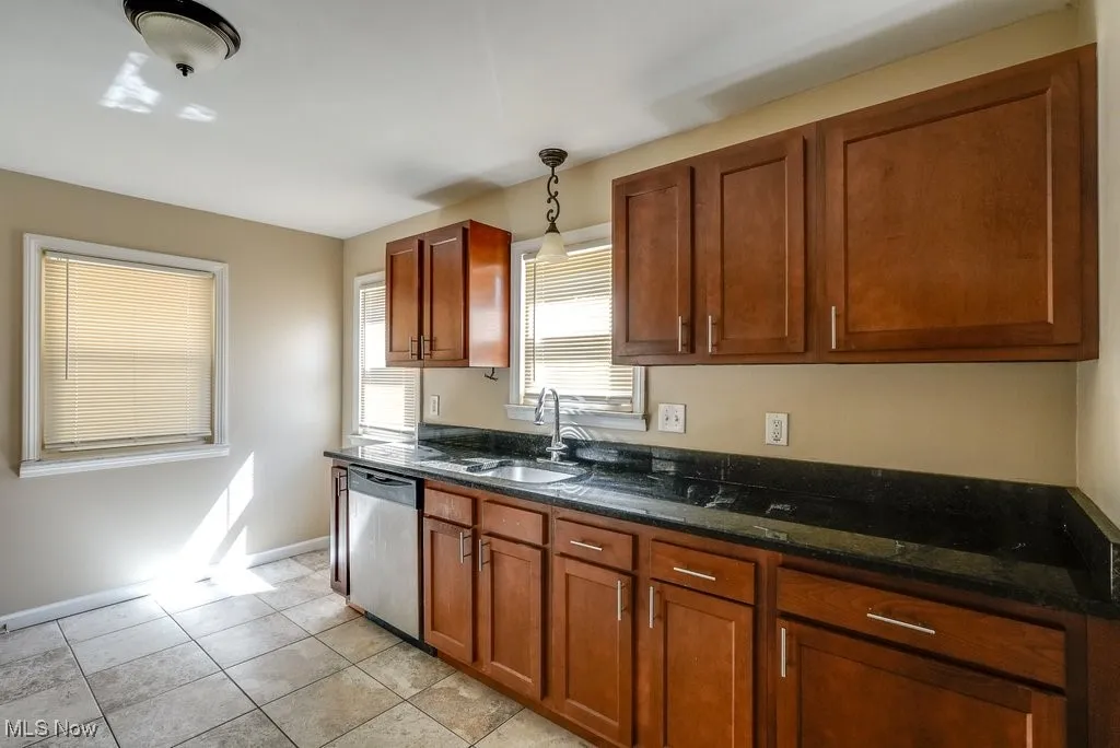 Kitchen with dishwasher, dark stone countertops, hanging light fixtures, and brown cabinets