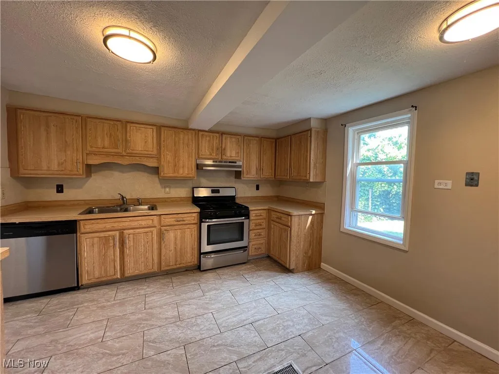 Kitchen with stainless steel appliances, under cabinet range hood, a textured ceiling, and light countertops