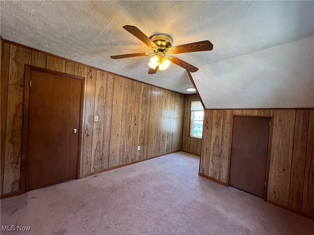 Additional living space with a textured ceiling, wood walls, ceiling fan, and carpet flooring