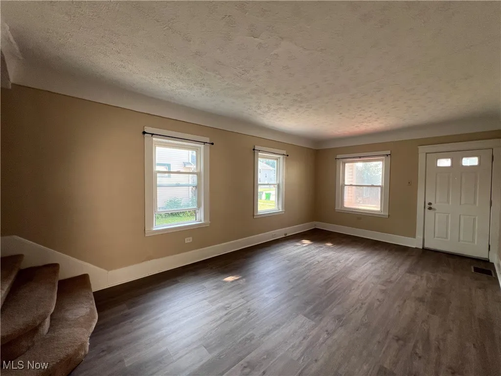 Unfurnished living room featuring a textured ceiling and dark wood-type flooring