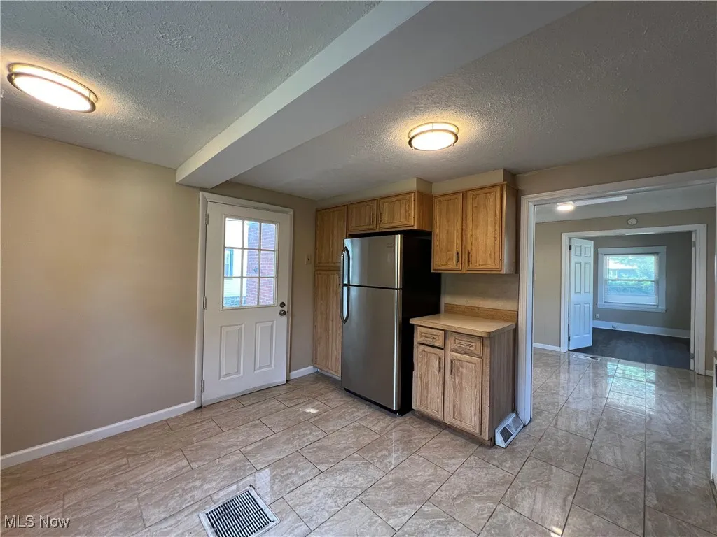 Kitchen featuring freestanding refrigerator, a textured ceiling, light countertops, and brown cabinetry