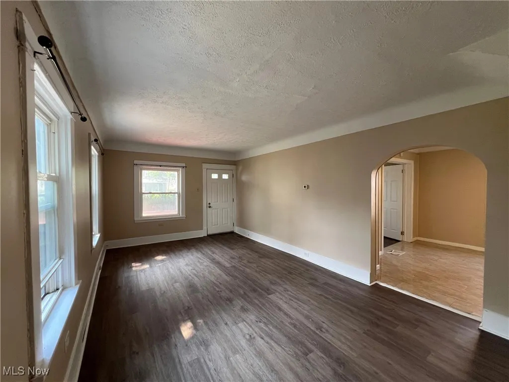 Unfurnished room featuring a textured ceiling, arched walkways, and dark wood finished floors