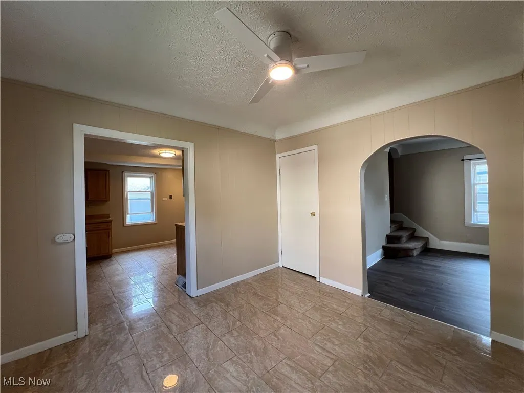 Unfurnished room with arched walkways, a ceiling fan, a textured ceiling, stairs, and ornamental molding