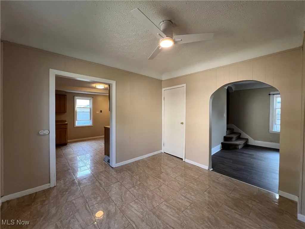 Empty room featuring arched walkways, a ceiling fan, a textured ceiling, stairway, and crown molding