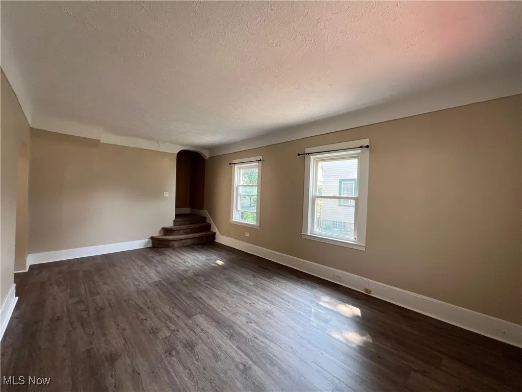 Spare room with a textured ceiling, dark wood-style floors, and arched walkways