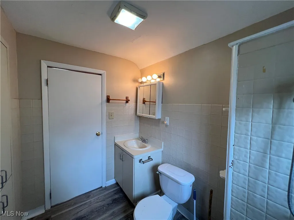 Bathroom featuring tile walls, vanity, wood finished floors, a shower stall, and wainscoting
