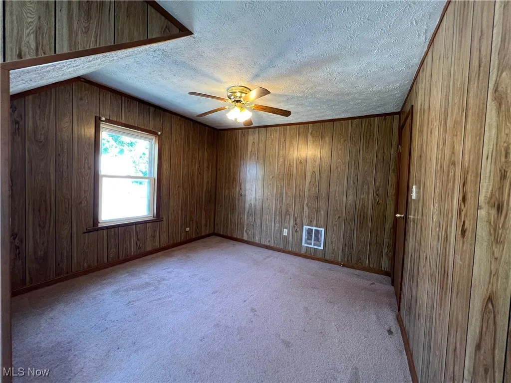 Unfurnished room with a textured ceiling, ceiling fan, light colored carpet, and wooden walls