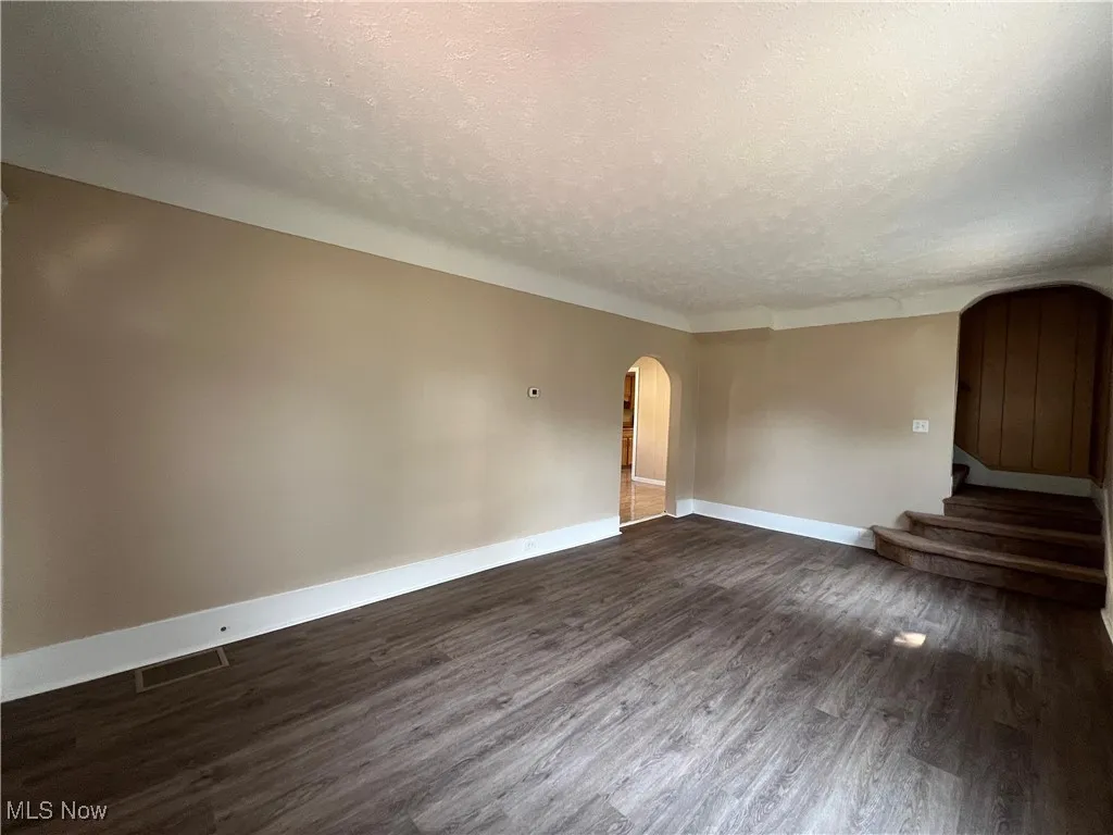 Empty room featuring arched walkways, a textured ceiling, dark wood-style floors, and stairs
