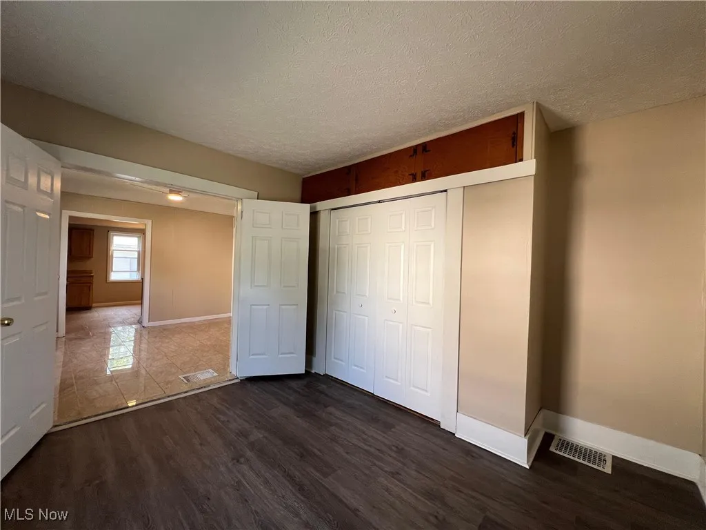 Unfurnished bedroom with dark wood-style flooring, a textured ceiling, and a closet