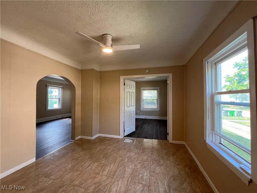 Empty room featuring healthy amount of natural light, a textured ceiling, a ceiling fan, and arched walkways