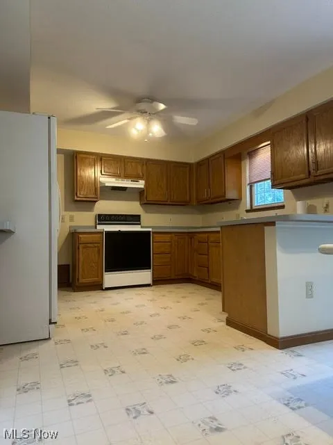 Kitchen featuring white appliances, under cabinet range hood, ceiling fan, and light flooring