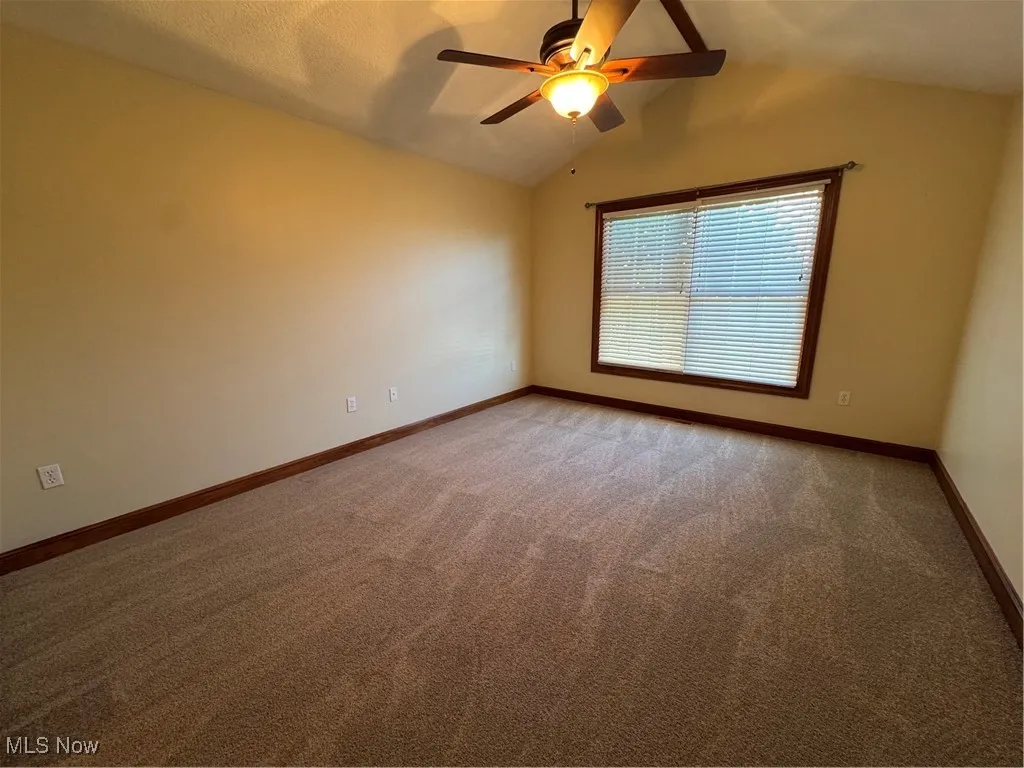 Carpeted spare room with lofted ceiling and ceiling fan