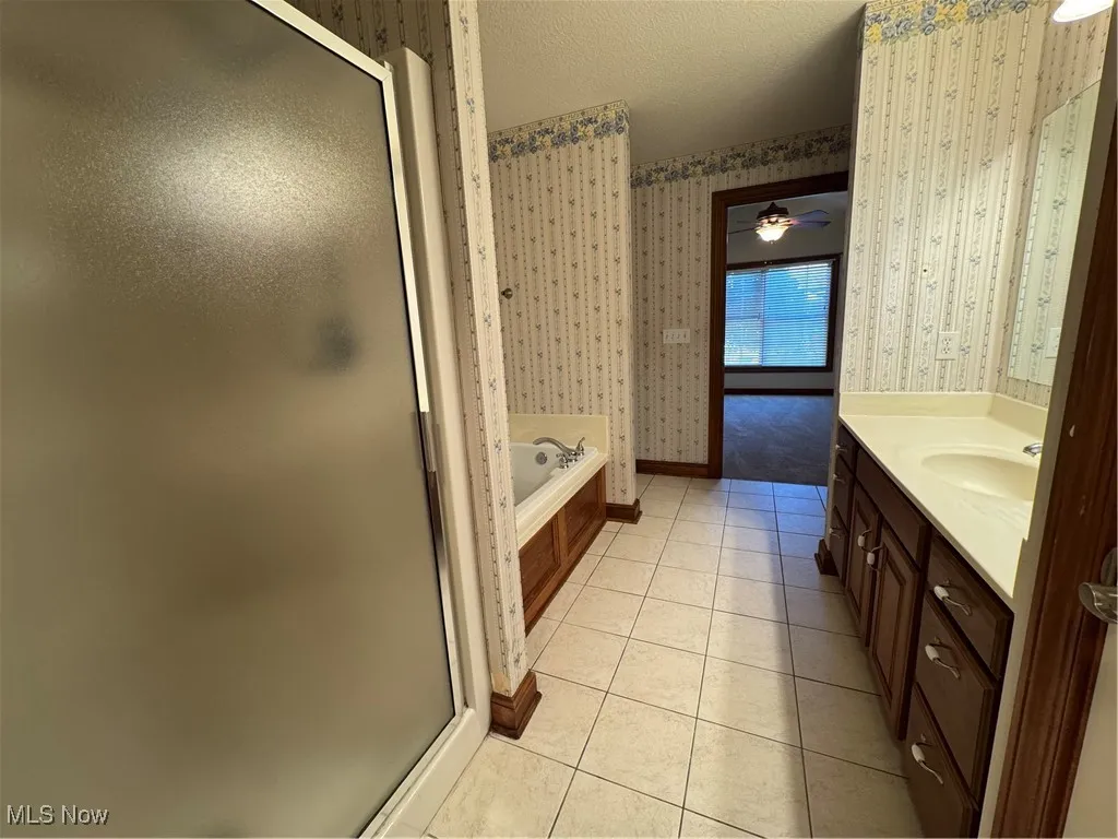 Bathroom featuring wallpapered walls, a shower stall, tile patterned floors, vanity, and a textured ceiling