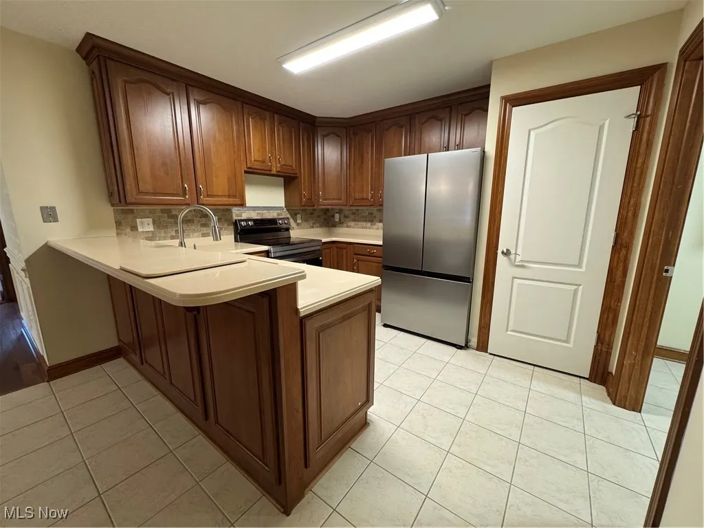 Kitchen with refrigerator, stove, a peninsula, light tile patterned floors, and light countertops