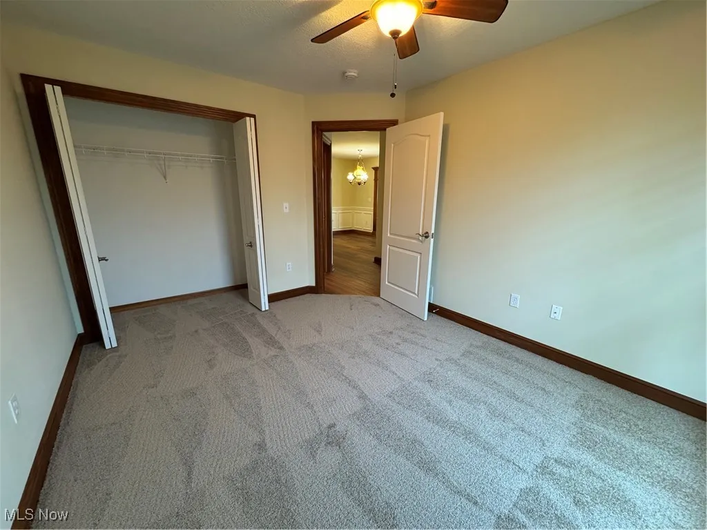 Unfurnished bedroom featuring light carpet, a chandelier, a closet, and a ceiling fan