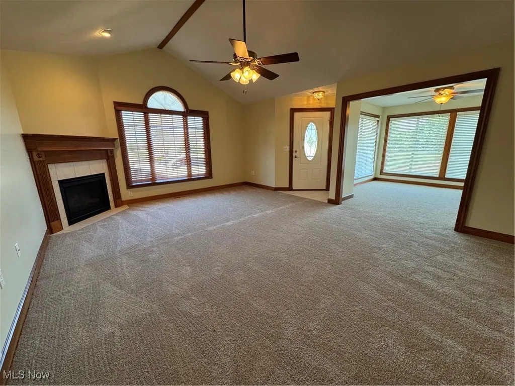 Unfurnished living room with ceiling fan, vaulted ceiling, carpet, and a tile fireplace