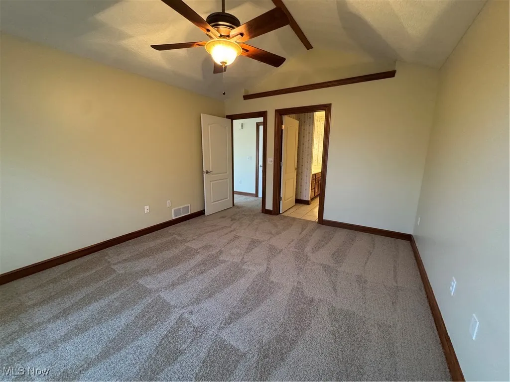 Unfurnished bedroom featuring lofted ceiling, light colored carpet, ensuite bathroom, and ceiling fan