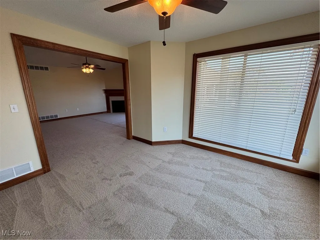 Empty room with a ceiling fan, light colored carpet, and a fireplace