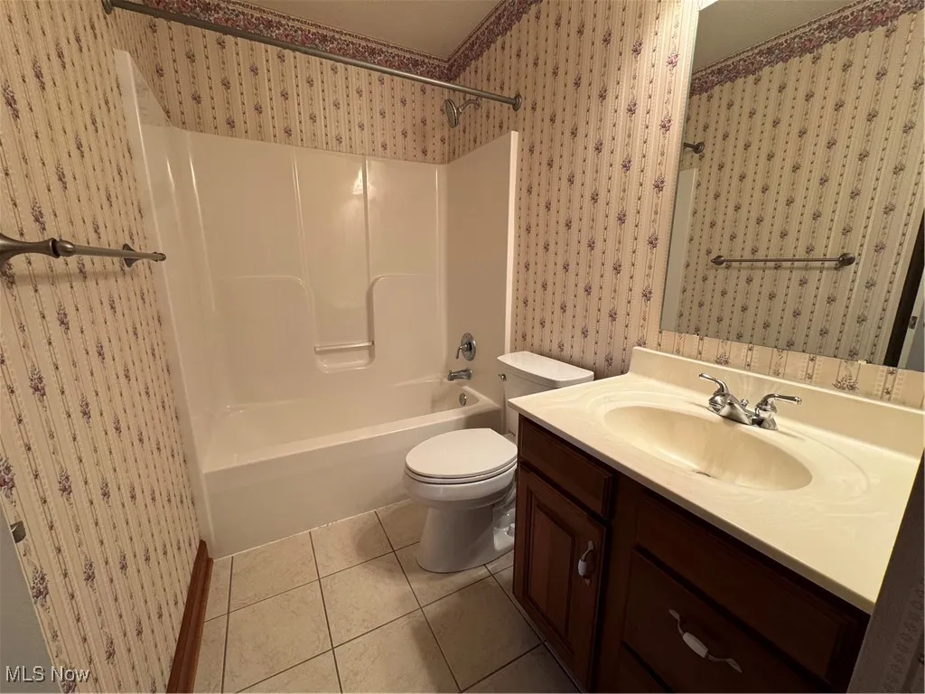 Bathroom with wallpapered walls, vanity, tile patterned flooring, and bathing tub / shower combination