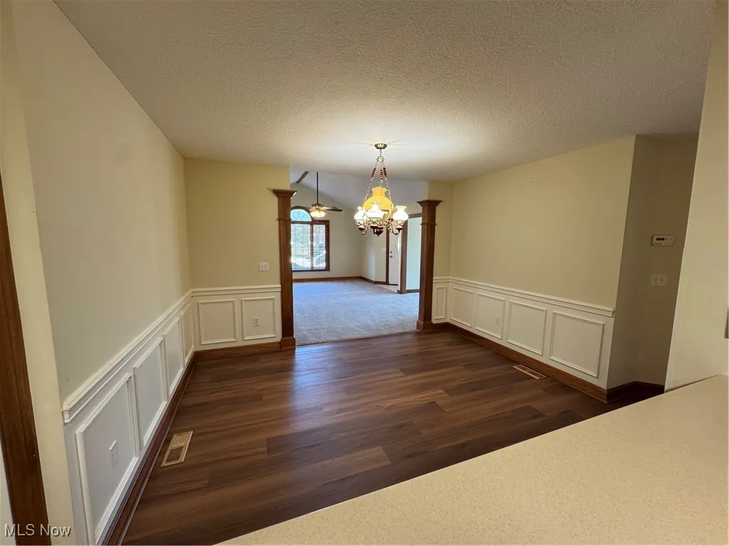 Unfurnished dining area featuring a decorative wall, decorative columns, a chandelier, dark wood-style floors, and a textured ceiling