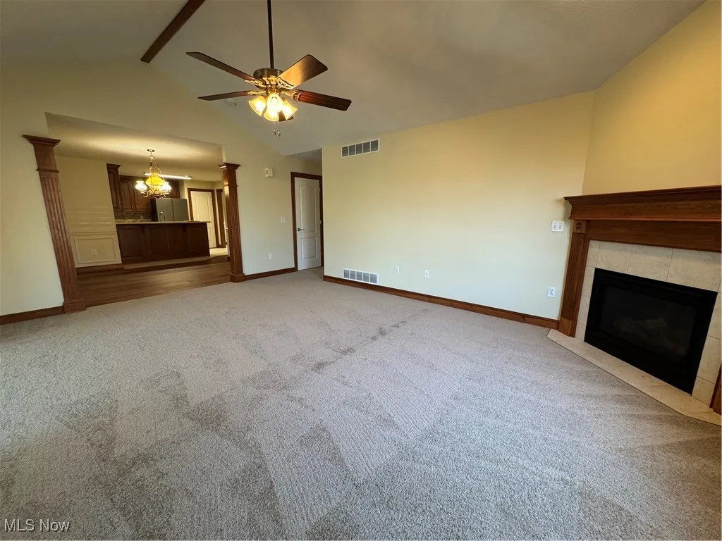 Unfurnished living room featuring a tiled fireplace, a ceiling fan, carpet floors, beamed ceiling, and high vaulted ceiling