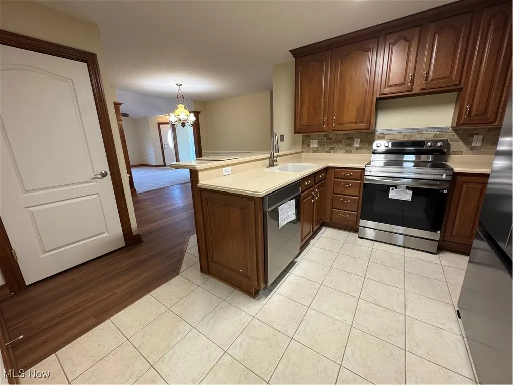 Kitchen with stove, dishwashing machine, a chandelier, a peninsula, and decorative backsplash