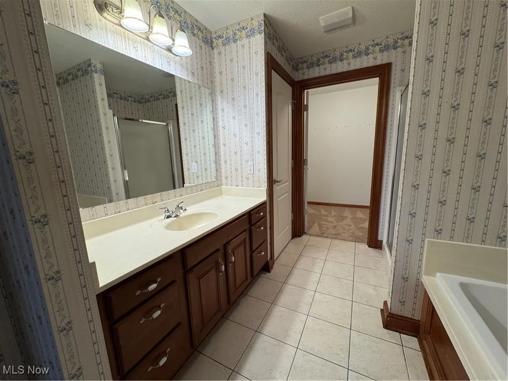 Bathroom with a stall shower, vanity, wallpapered walls, tile patterned flooring, and a garden tub
