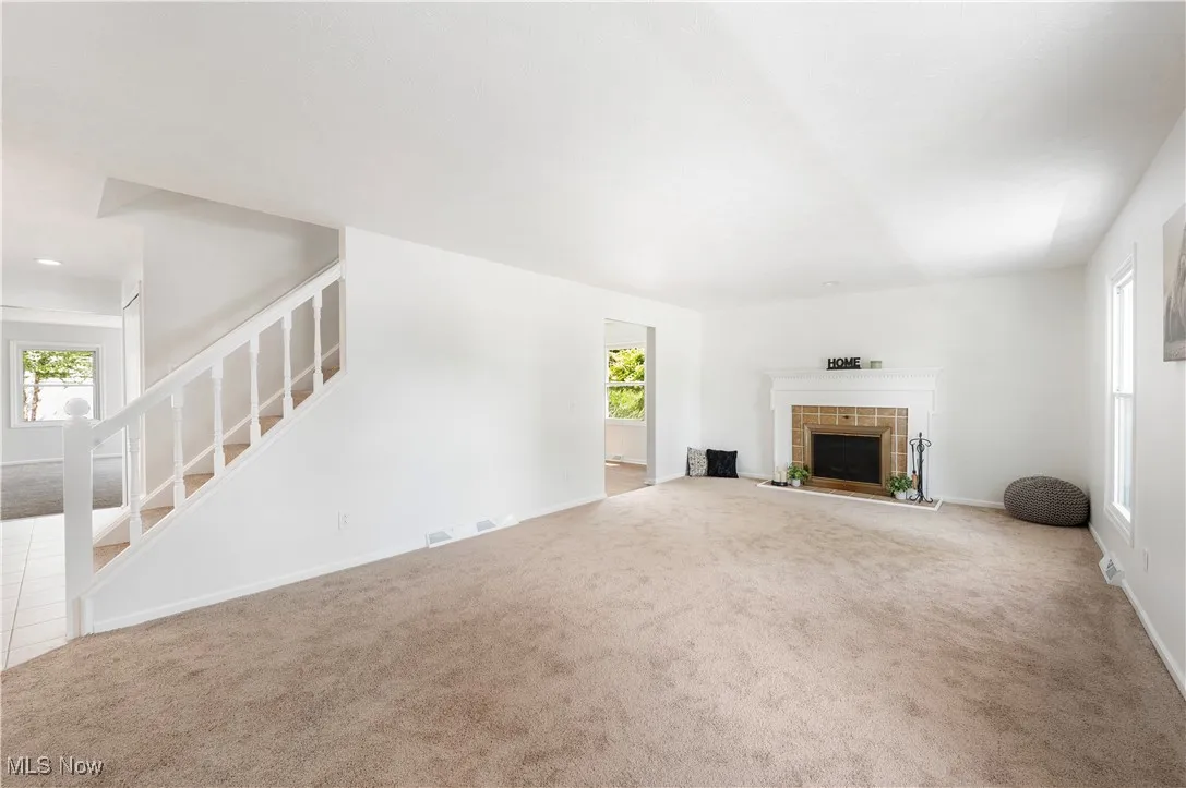 Unfurnished living room with carpet, stairway, and a tile fireplace