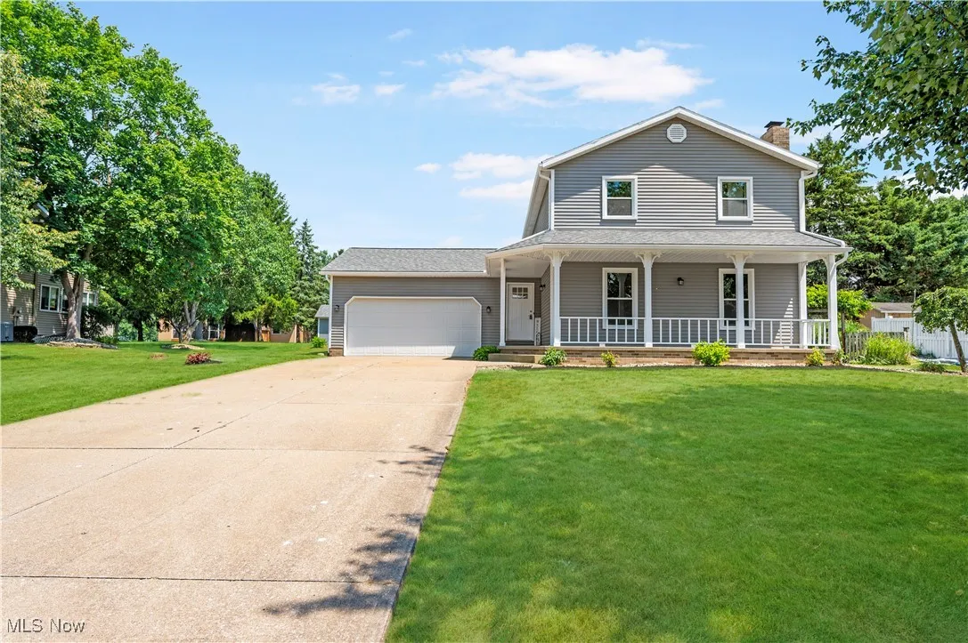 View of front of home featuring concrete driveway, a garage, a front lawn, a porch, and a chimney