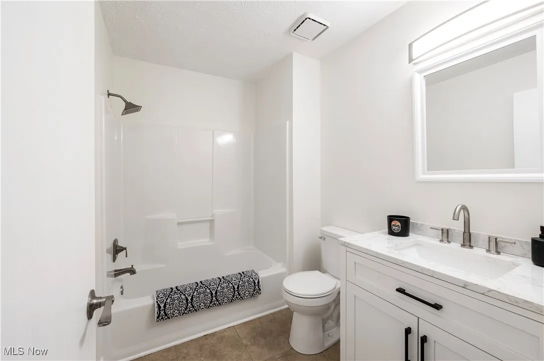 Full bathroom featuring vanity, shower / tub combination, tile patterned flooring, and a textured ceiling