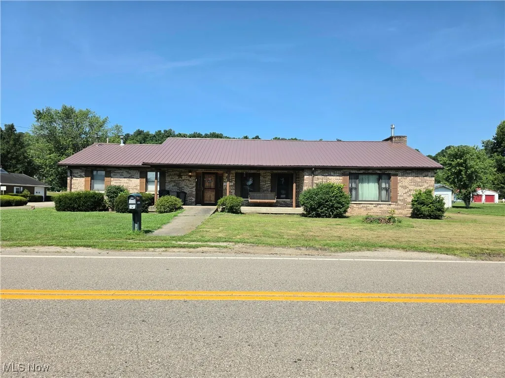 Single story home featuring a metal roof, a front lawn, and brick siding