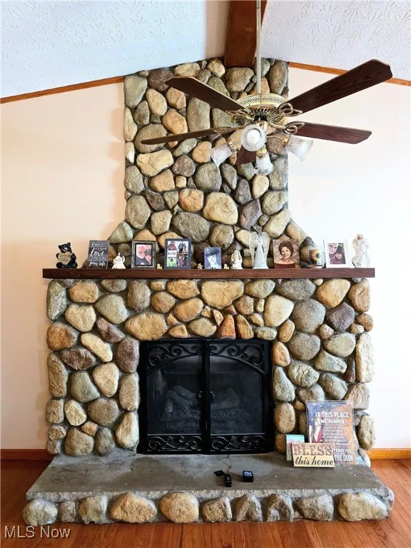 Detailed view of a stone fireplace, ceiling fan, wood finished floors, and a textured ceiling