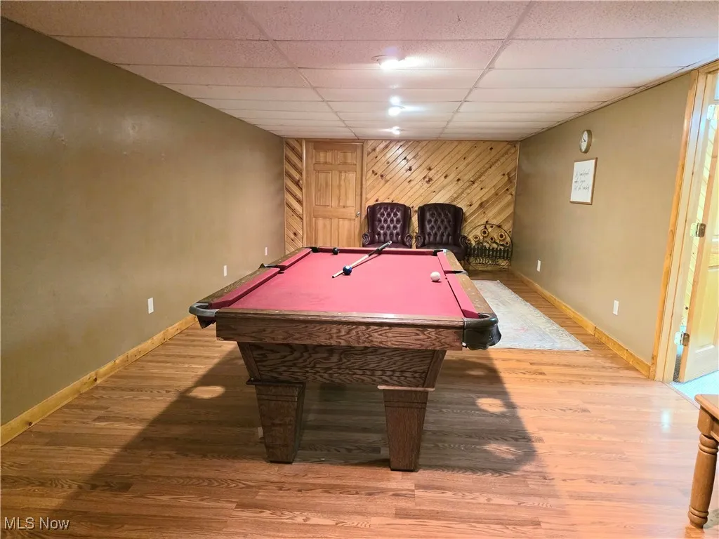 Game room featuring light wood-style flooring, billiards, a paneled ceiling, and wood walls
